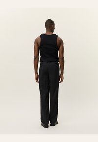 Black sleeveless top paired with grey tailored trousers. The fabric is smooth, with a straight fit and subtle texture. Black shoes complete the look.