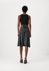 Fekete cropped tank top, egy laza, bokáig érő sötétszürke szoknyával, derékhoz kötővel és puha, texturált felülettel. Blokkos sarkú szandálok.