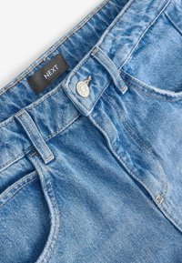 Jeans in denim blu chiaro con design classico a cinque tasche, una robusta chiusura con bottone e cuciture a contrasto. L'etichetta riporta "NEXT."