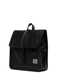 Mochila negra hecha de material duradero, con cierre de solapa, correa ajustable y una etiqueta frontal que detalla la marca. Textura suave.