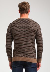 Strick-Pullover mit einem dunkelbraunen und goldenen geometrischen Muster, gerippten Bündchen und Saum sowie einem Rundhalsausschnitt. Strukturiertes Material.