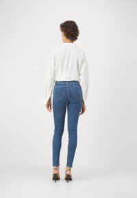 Blå denim skinny jeans med hög midja, bakfickor och smal passform, kombinerat med en vit långärmad skjorta och svarta klackar.