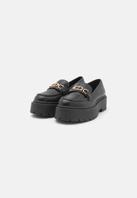 Zwarte leren platform loafers met een chunky zool en een gouden kettingaccent aan de voorkant. Glad textuur en afgeronde neusdesign.