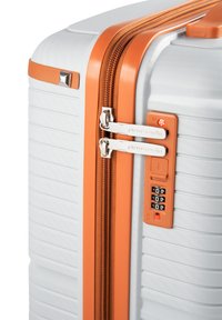 Maleta rígida con un acabado texturizado blanco y acentos naranjas. Presenta cremalleras dobles y una cerradura de combinación en el lateral.