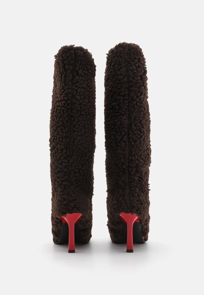 Botas de tacón alto marrones, con un material texturizado y peludo, caña alta y distintivos tacones de aguja rojos. Base negra sólida.