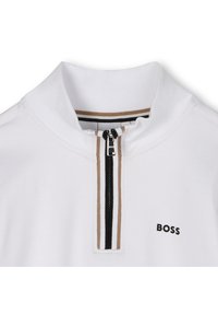 Camisa polo branca com colarinho alto e fecho de zip. Acentuada com riscas pretas e castanhas. Logótipo "BOSS" em preto no lado esquerdo.