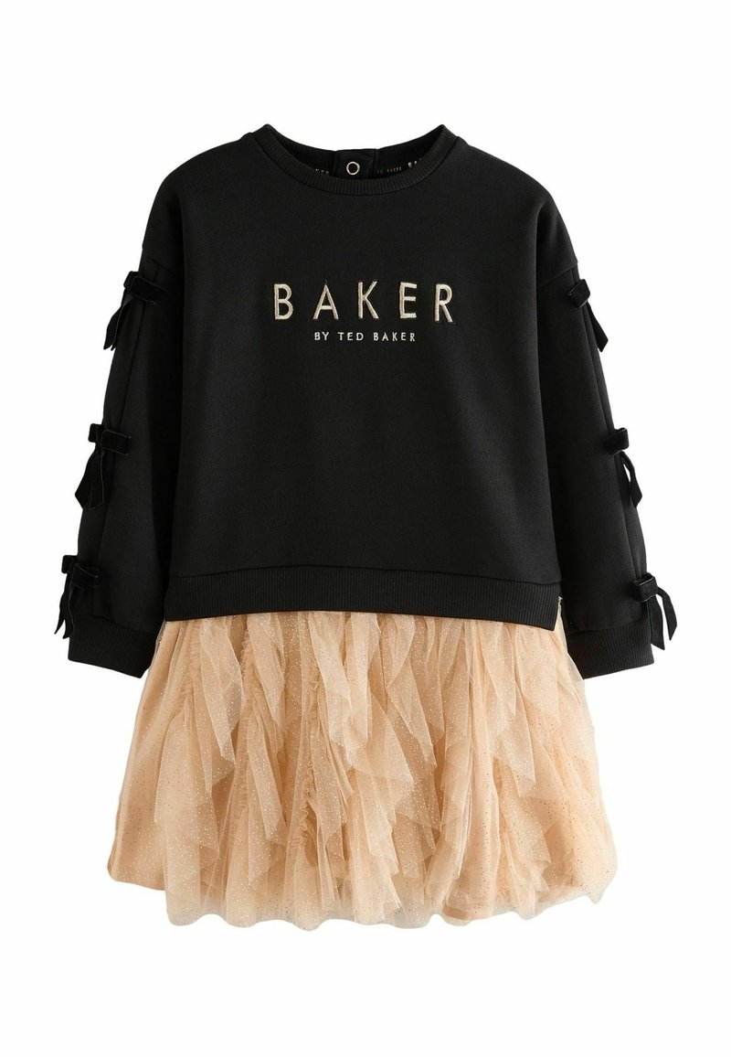 Musta huppari, jossa on kultainen "BAKER"-logo, hihoissa nauha-koristeet; kiinnitetty beige tüllihame, jossa on kerroksellinen, röyhelöinen rakenne.
