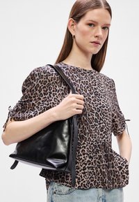 Μαύρη δερμάτινη τσάντα με λεία υφή, με στρογγυλό σχήμα. Συνδυασμένη με μπλούζα με λεοπάρ σχέδιο.