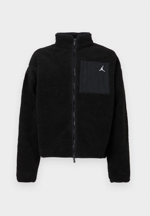 Črna flis jakna z visokim ovratnikom, polnim zadrgo in sprednjim žepom. Ima bel Jordan logotip na žepu. Mehka, strukturirana tkanina.