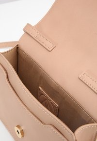 Jasnobeżowa torebka skórzana o gładkiej fakturze, z zapięciem na zatrzask w kolorze złotym oraz wewnętrzną kieszenią. Czysty, minimalistyczny design.