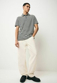 Una polo a maniche corte presenta un motivo a scacchi bianco e nero, abbinata a pantaloni crema dalla vestibilità comoda e scarpe nere con suola spessa.