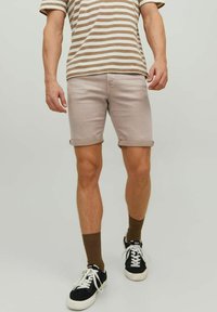 Pantalones cortos de mezclilla color beige claro con dobladillos enrollados, combinados con una camiseta a rayas en marrón y blanco, y zapatillas negras con suelas blancas.