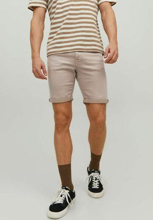 Pantalones cortos de mezclilla color beige claro con dobladillos enrollados, combinados con una camiseta a rayas en marrón y blanco, y zapatillas negras con suelas blancas.
