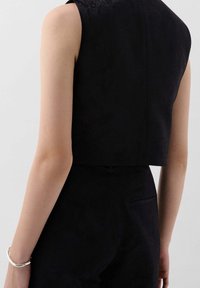 Svart, kortärmad topp utan ärmar med en strukturerad yta, med hög halsringning och rak bakdel. Enkelt design med rena linjer.