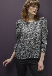 Blusa de padrão abstrato em preto e branco, com mangas bufantes, tecido leve e decote arredondado, combinada com calças pretas.