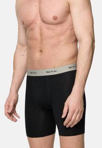 Svarta boxertrosor i slät tyg med ett grått elastiskt midjeband som har svart text. Slimmad design med medellång längd till låret.