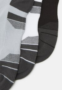 Tre paia di calzini in grigio, bianco e nero. Ogni paio presenta righe a contrasto e textures a coste, mettendo in mostra un design morbido e lavorato a maglia.