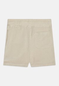 Beige Shorts aus weichem Stoff mit einem elastischen Bund, ausgestattet mit einer einzelnen Gesäßtasche und einer strukturierten Oberfläche.