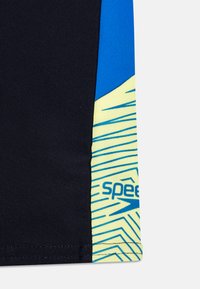 Pantaloni da nuoto Speedo con base blu navy, pannello accentato blu e gradiente giallo con motivi a zigzag. Logo stampato sul lato.