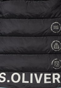 Schwarze Daunenjacke mit horizontalem Steppmuster. Enthält weißen Text und Icons, die Materialien und Pflegehinweise anzeigen. Aus recyceltem Polyester.