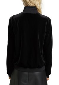 Czarna aksamitna kurtka zapinana na suwak z wysokim kołnierzem, miękką fakturą, ściągaczami na mankietach i u dołu oraz luźnym krojem i minimalistycznym wzornictwem.