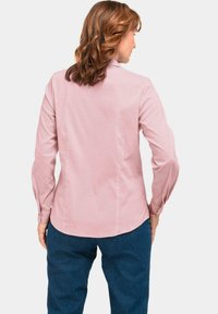 Button-up-Hemd aus weichem rosa Stoff mit klassischem Kragen, langen Ärmeln und abgerundetem Saum, kombiniert mit dunkelblauen Jeans.