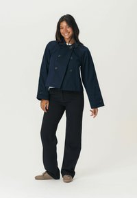 Tumši zils kropts divrindu žakets ar lieliem melniem pogām, savienots ar melnām biksēm. Gluda auduma struktūra, plašas piedurknes.