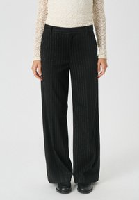 Pantalons noirs à rayures avec une coupe large, en tissu texturé et avec des accents métalliques subtils, assortis à un haut ajusté.