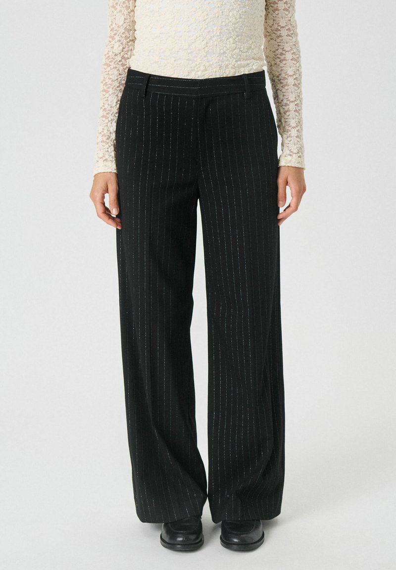 Pantalons noirs à rayures avec une coupe large, en tissu texturé et avec des accents métalliques subtils, assortis à un haut ajusté.