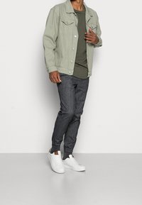 Světlá zelená džínová bunda přes tmavě zelené tričko, spárovaná s tmavě šedými teplákovými kalhotami a bílými teniskami. Klasický střih a moderní design.