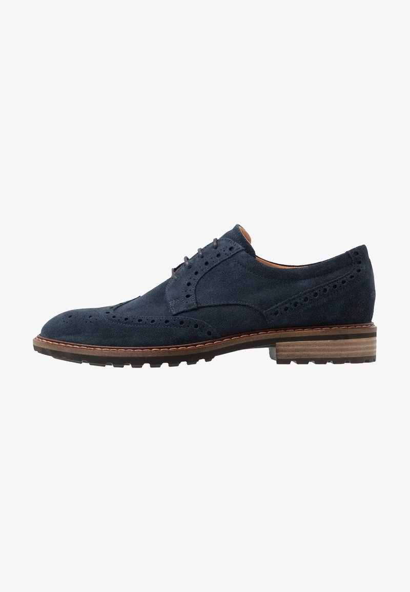 Chaussure brogue homme en daim bleu marine avec design à bout rapporté, détails perforés, talon empilé marron et semelle en caoutchouc noire.