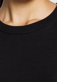 Suéter negro de punto con escote redondo y textura acanalada, que muestra detalles finos en el entrelazado de la tela y su suavidad.