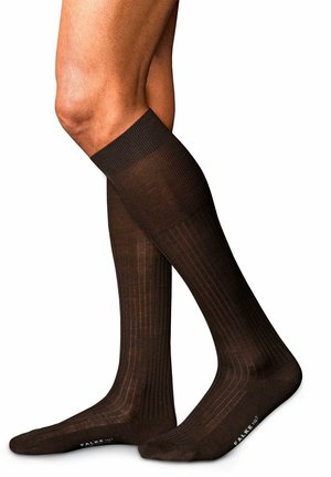 Calcetas marrones hasta la rodilla con textura acanalada y diseño sólido. Presentan una puntera redondeada y un talón reforzado con el logo de la marca en la suela.