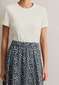 Krämfärgad, ribbad kortärmad topp som kombineras med en svart kjol med ett blått grafiskt mönster, elastisk midja och flödande design.