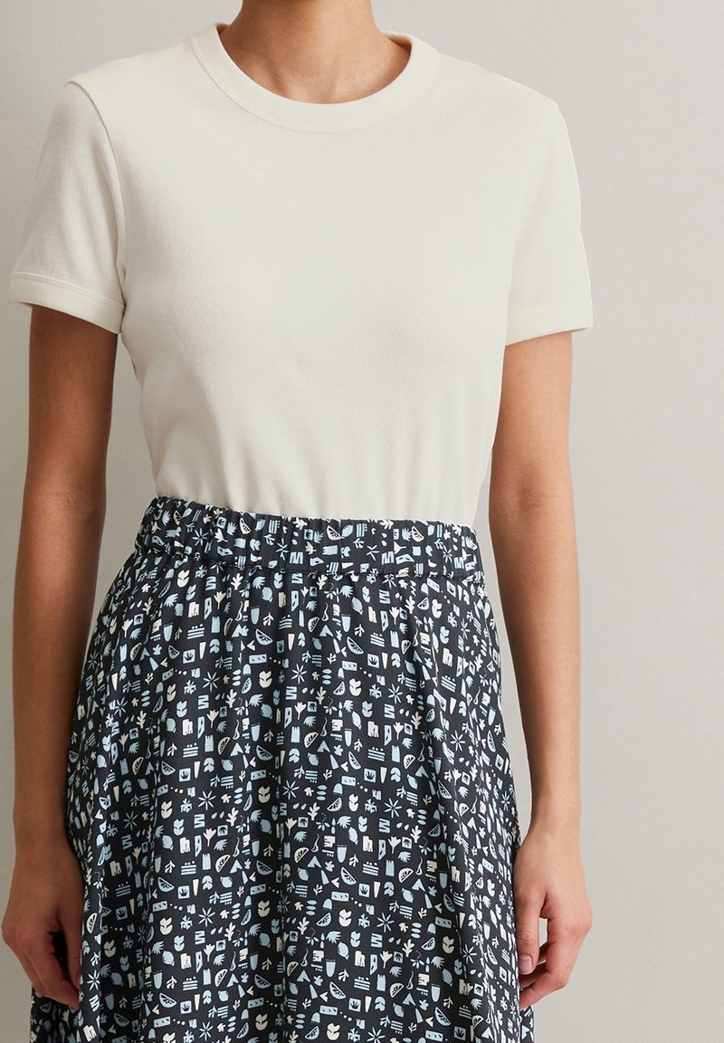 Krämfärgad, ribbad kortärmad topp som kombineras med en svart kjol med ett blått grafiskt mönster, elastisk midja och flödande design.