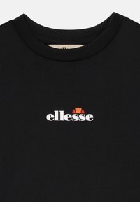 Čierne bavlnené tričko s okrúhlym výstrihom, jemnou textúrou a bielym logom "ellesse" s červenou a oranžovou grafikou nad ním.