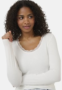 Långärmad vit topp, ribbad textur, med ett vågigt spetskrage. Fitted design, slät tyg, med en lätt stretch.
