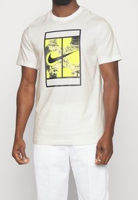 Camiseta de algodón blanca con un gran gráfico de Nike en amarillo y negro dentro de un marco rectangular en el frente. Manga corta, cuello redondo.