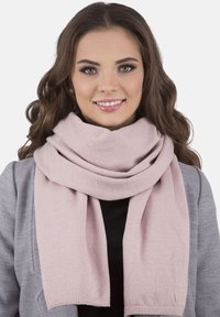 Eșarfă tricotată de un roz deschis, cu o textură moale, așezată în jurul gâtului, asociată cu un palton gri și un top negru pentru un aspect stratificat.