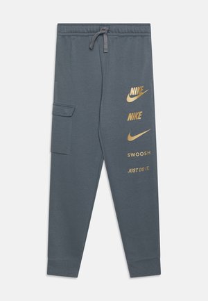 Ciemnoszare spodnie dresowe Nike z elastycznym pasem, ściągaczem, boczną kieszenią typu cargo oraz złotymi logo Nike i napisem na prawej nogawce.