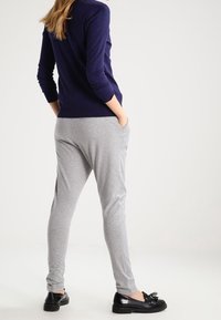 Pantalones de chándal grises con un ajuste relajado, confeccionados en tejido suave. Combinados con un suéter azul marino y mocasines negros, mostrando cintura elástica y bolsillos laterales.