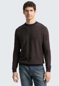 Donkergepatteerde gebreide sweater met een ronde halslijn, ribgebreide manchetten en een zoom. Draagt met blauwe jeans, gemaakt van een textuurstof.