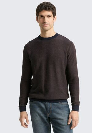 Maglione a maglia con motivo scuro, collo a giro, polsini e orlo a coste. Indossato con jeans blu, caratterizzati da un tessuto testurizzato.