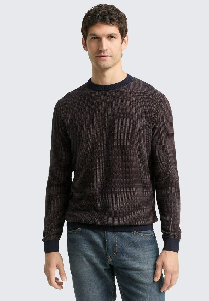 Donkergepatteerde gebreide sweater met een ronde halslijn, ribgebreide manchetten en een zoom. Draagt met blauwe jeans, gemaakt van een textuurstof.