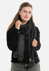 Zwarte en grijs gestreepte sjaal gemaakt van een zachte stof, met geometrische ontwerpen en franjes, casual om de nek van een persoon gedrapeerd.