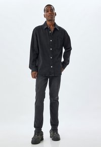 Chaqueta de mezclilla negra con cierre de botones y bolsillo, combinada con jeans negros a juego y zapatillas negras gruesas con detalles.