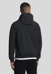 Sort hættejakke med en blød tekstur, elastiske manchetter og en kant. Den har et enkelt, strømlinet design uden synlige logoer eller udsmykninger.