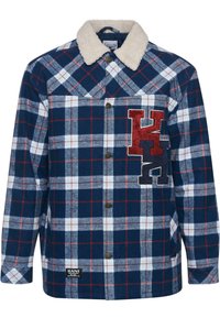 Marineblå og hvidternet flannel skjorte med en beige sherpa-krave, prydet med broderede røde og sorte bogstaver på brystet og brune knapper.