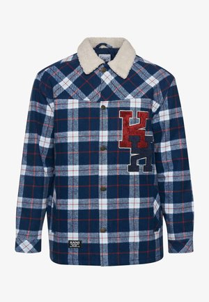 Camisa de franela a cuadros en azul marino y blanco con un cuello de sherpa beige, que presenta letras bordadas en rojo y negro en el pecho y botones marrones.