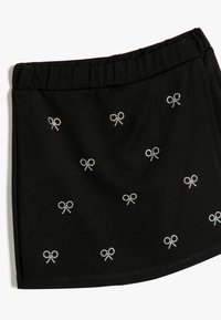 Jupe noire avec une taille élastique, ornée de petits nœuds en strass disséminés sur le tissu. Texture douce.